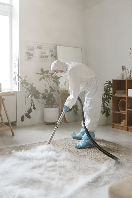 A person kneeling on a patterned carpeted floor, using a yellow and black vacuum cleaner with a flexible hose for surface cleaning. The individual, wearing blue jeans and a beige top, is placing a clo